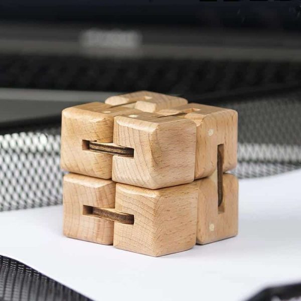 Cubo de madeira com encaixes que permite criar uma estrutura infinita, visto de cima com fundo de superfície branca e elementos de escritório ao fundo.