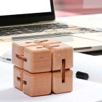 Cubo de madeira com encaixes articulados, visto de frente com um computador portátil ao fundo.