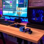 Cubo Infinito Galáxia com efeito de estrelas, colocado numa mesa de gaming com computador e acessórios iluminados a LED azul.