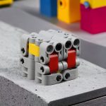 Cubo Infinito LEGO com peças cinzentas, vermelhas e amarelas, visto de cima, com detalhes das conexões e encaixes.