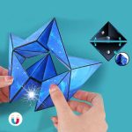 Pessoa a montar o Cubo Infinito Origami com peças de plástico decoradas com imagens de espaço e relâmpagos, mostrando detalhes das junções e componentes internos.