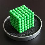 Cubo de esferas verdes luminosas empilhadas formando um cubo, colocado numa caixa com interior preto, visto de cima.
