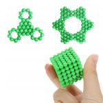 Conjunto de esferas verdes formando diferentes figuras geométricas, incluindo um cubo e uma estrela, com uma mão segurando um cubo de esferas.