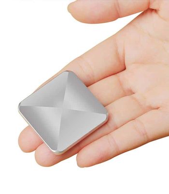 Pequeno objeto de metal prateado com forma quadrada e superfície lisa, segurado na palma da mão de uma pessoa.