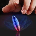 Dedo a tocar um cristal de plasma com efeito de luzes azuis, roxas e vermelhas, refletindo na superfície escura.