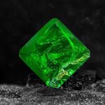 Cristal de quartzo verde com superfície brilhante e textura detalhada, colocado sobre uma base escura com fundo desfocado.