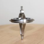 Giroscópio de metal com estrutura circular e eixo central, colocado sobre uma superfície de madeira, mostrando detalhes do seu design técnico.