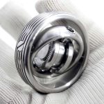 Giroscópio Fidget Spinner de metal com design circular e detalhes internos visíveis, segurado por uma mão com luva branca.