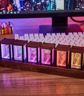 Relógio Nixie com seis tubos de vidro iluminados em cores diferentes, montado numa base de madeira, com fundo de computador e teclado.
