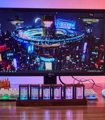 Monitor de computador com fundo de cidade futurista e relógio Nixie em destaque na base, com teclado e caneta ao lado.