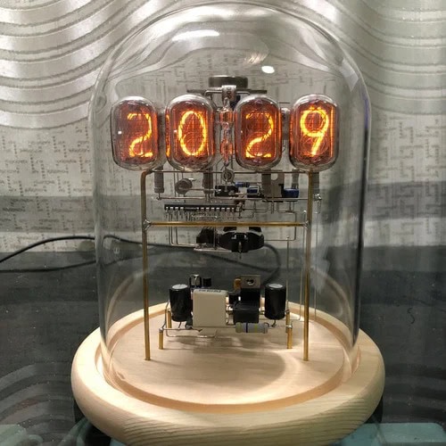 Relógio Nixie com tubos de néon exibindo o ano 2029, visível através de uma cúpula de vidro, com componentes eletrónicos internos e base de madeira.