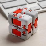 Cubo Infinito com peças brancas e vermelhas, mostrando detalhes de encaixe e movimento, colocado sobre uma superfície de escritório com teclado ao fundo.