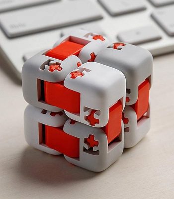 Cubo Infinito com peças brancas e vermelhas, mostrando detalhes de encaixe e movimento, colocado sobre uma superfície de escritório com teclado ao fundo.