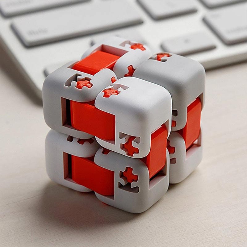 Cubo Infinito com peças brancas e vermelhas, mostrando detalhes de encaixe e movimento, colocado sobre uma superfície de escritório com teclado ao fundo.