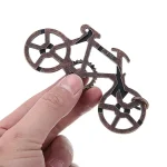 Pequeno puzzle metálico de uma bicicleta, visto de perto, com detalhes das rodas e quadro, sendo segurado por uma mão.