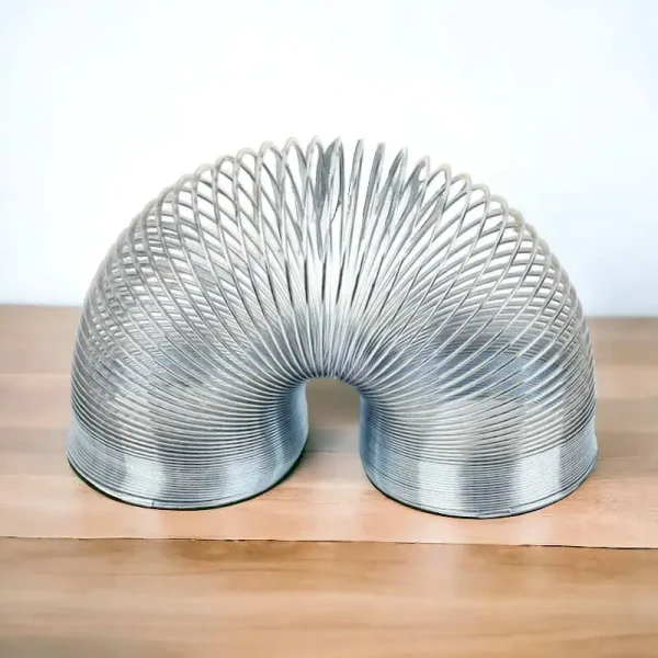 Mola Slinky metálica em forma de U vista de cima, com detalhes das espirais e acabamento brilhante, colocada sobre uma superfície de madeira clara.