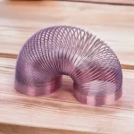 Mola Slinky metálica de cor prateada, em forma de espiral, colocada sobre uma superfície de madeira clara, mostrando detalhes do seu design.