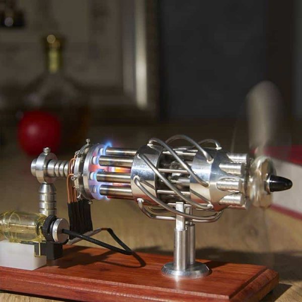 Motor Stirling metálico com tubos de calor, componentes de metal brilhante, em funcionamento, com chama visível na câmara de combustão, montado numa base de madeira.