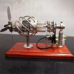 Modelo de motor Stirling com componentes metálicos, tubos de vidro e hélice, montado numa base de madeira, usado para demonstrações científicas.