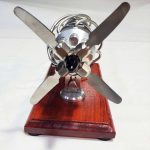 Motor Stirling compacto com hélices de metal, montado numa base de madeira, usado para demonstrações científicas e educativas.
