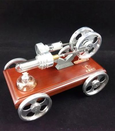Modelo de motor Stirling em miniatura com rodas de metal, base de madeira e componentes de vidro e metal, exibido numa superfície escura.