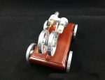 Motor Stirling compacto com rodas de metal, componentes de cobre e estrutura de madeira, usado em demonstrações científicas.