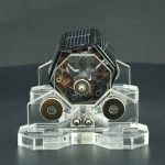 Modelo de motor Stirling solar com painéis solares, componentes metálicos e estrutura de acrílico transparente, exibido numa base de suporte.