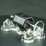 Mini motor Stirling alimentado por energia solar, com painel solar fotovoltaico e estrutura de suporte transparente, demonstrando energia renovável.