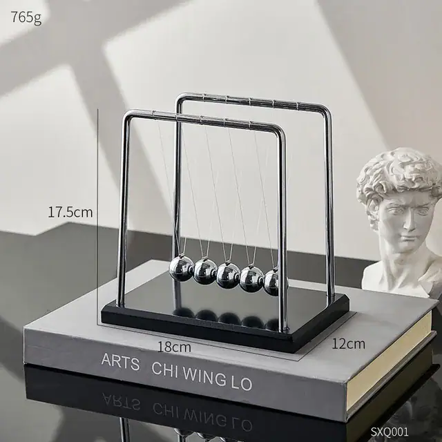 Pêndulo de Newton com cinco bolas de metal suspensas por fios finos, estrutura de metal e base de madeira escura, colocado sobre um livro de ciência.