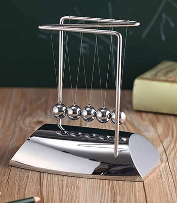 Pêndulo de Newton com bolas de metal suspensas por fios finos, base metálica brilhante, em ambiente de sala de aula ou escritório.