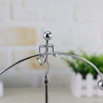 Pêndulo de Newton com bolas de metal suspensas por fios finos, mostrando o movimento de uma bola ao ser puxada.