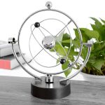 Pêndulo de Newton com esferas de metal suspensas por fios finos, mostrando movimento de balançar, em ambiente de escritório com plantas e livros ao fundo.
