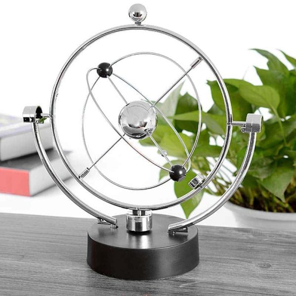 Pêndulo de Newton com esferas de metal suspensas por fios finos, mostrando movimento de balançar, em ambiente de escritório com plantas e livros ao fundo.
