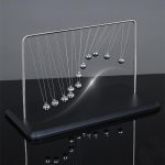 Pêndulo de Newton gigante com bolas metálicas suspensas por fios finos, exibindo movimento de colisão e energia.