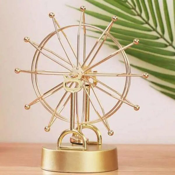 Pêndulo de Newton com esfera de metal dourada, rodas e hastes em disposição radial, sobre base dourada, com folha de palmeira ao fundo.
