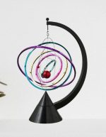 Modelo de sistema solar com órbitas coloridas e esfera vermelha representando o Sol, suspenso por fios em estrutura de suporte preto.