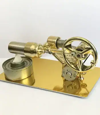Motor Stirling em miniatura com rodas e componentes metálicos dourados, montado numa base dourada, mostrando detalhes do mecanismo interno e externo.