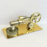 Motor Stirling em miniatura com rodas e componentes metálicos dourados, montado numa base dourada, mostrando detalhes do mecanismo de funcionamento.