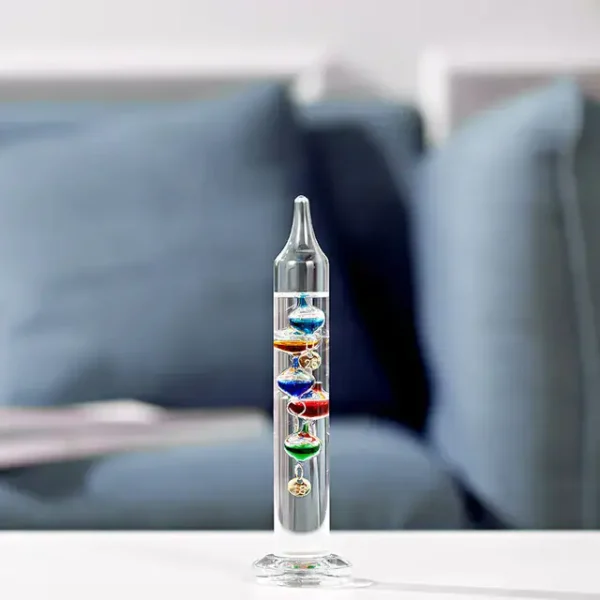 Termómetro de Galileu com várias bolhas de cores diferentes, visível em fundo de sofá azul claro.
