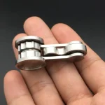 Pequena cadeia de metal com elos articulados, vista de perto, sobre fundo escuro, mostrando detalhes de acabamento e ligação entre os elos.