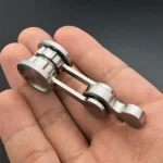 Peça de metal com componentes cilíndricos e braços metálicos, usada em experimentos científicos ou demonstrações educativas.