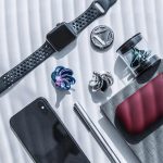 Relógio inteligente, auriculares, smartphone, e acessórios de ciência em uma mesa com luz natural.