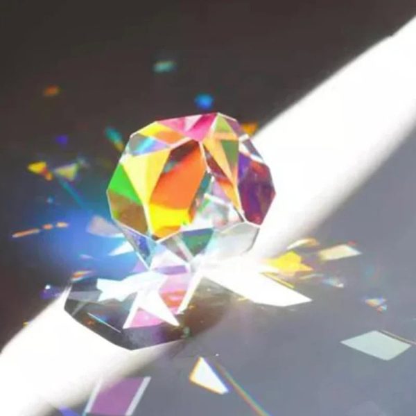 Cubo de cristal transparente com múltiplos ângulos que reflete luz, criando efeitos de cores no chão ao lado.