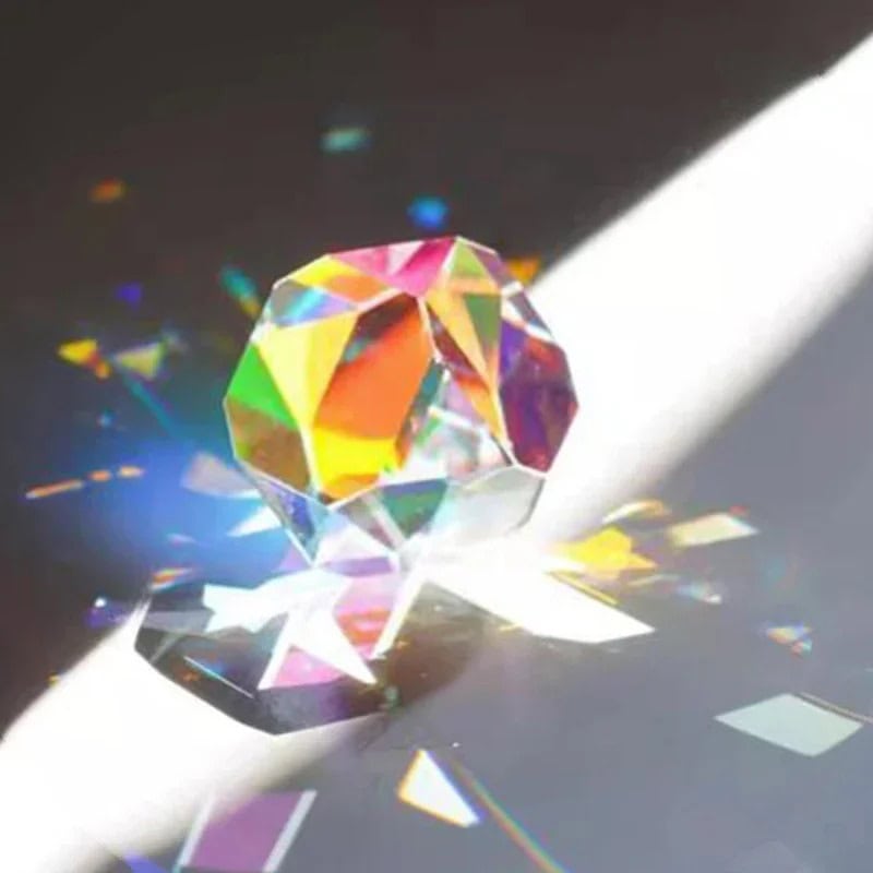 Cubo de cristal transparente com múltiplos ângulos que reflete luz, criando efeitos de cores no chão ao lado.