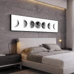 Painel com imagens das fases da lua, do novo ao cheio, pendurado na parede de um quarto moderno com cama de casal e iluminação suave.