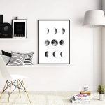 Quadro com várias fases da Lua em preto e branco pendurado na parede branca de um espaço de estar.