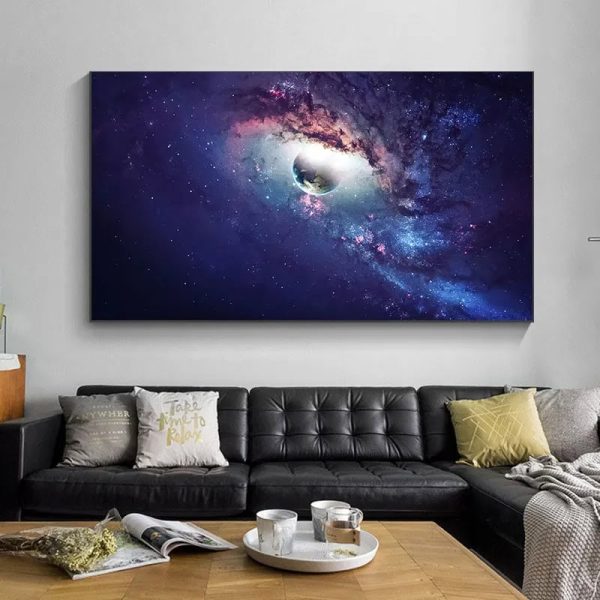 Painel de parede com imagem de uma nebulosa colorida e um planeta em destaque, decorando uma sala moderna com sofá preto e almofadas.