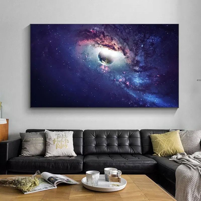 Painel de parede com imagem de uma nebulosa colorida e um planeta em destaque, decorando uma sala moderna com sofá preto e almofadas.