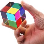 Pessoa segurando um cubo de prisma óptico com cores vibrantes e faces transparentes, mostrando diferentes ângulos e reflexões.
