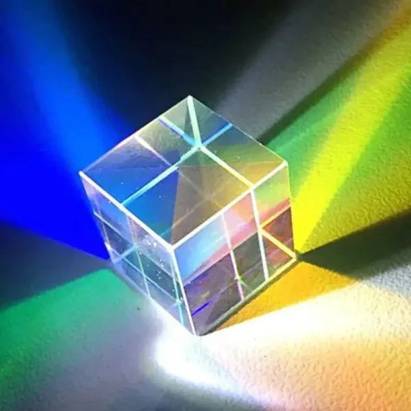 Cubo de vidro transparente com prismas internos que dispersam a luz em cores do espectro visível, projetando um arco-íris de luz na superfície.